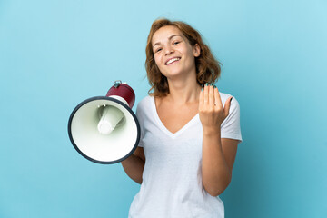 Young Georgian woman isolated on blue background holding a megaphone and inviting to come with hand