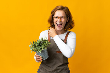 Young Georgian woman holding a plant isolated on yellow background celebrating a victory
