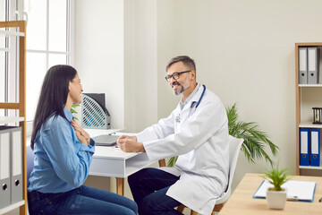 Male doctor consulting female patient in medical clinic. Positive professional physician talking to smiling young woman at medical check up visit. Healthcare and medical treatment concept