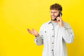 Young handsome caucasian man isolated on yellow background keeping a conversation with the mobile phone with someone