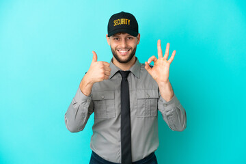 Young security man isolated on blue background showing ok sign and thumb up gesture