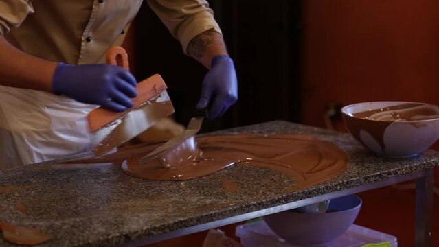 A man in apron skillfully stirs milk chocolate on a marble tabble