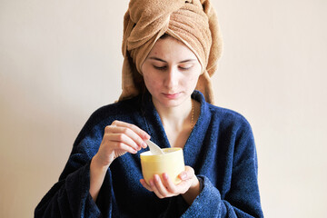 woman in a robe and with a towel on her head applies cosmetics to skin