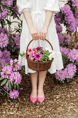 Basket with flowers in hands and rhododendron bushes.