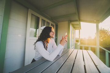 a woman sitting on the terrace of a bungalow with the mobile at sunset