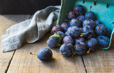 Carton of fresh picked plums spilled onto wooden background.
