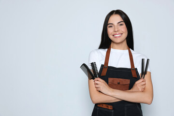 Portrait of happy hairdresser with professional combs on light background, space for text