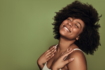 Delighted young black lady smiling with closed eyes against green background