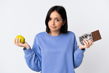 Young caucasian woman isolated on white background having doubts while taking a chocolate tablet in...