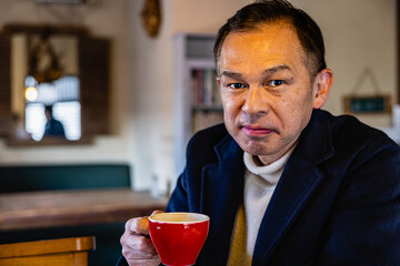 Middle-aged Asian man drinking coffee alone in the cafeteria.