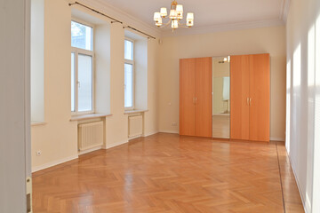 A hall in an empty bright apartment with large windows and a shiny floor.