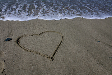Fototapeta na wymiar Heart on the beach. The sea wave washes away the heart drawn on the sand.