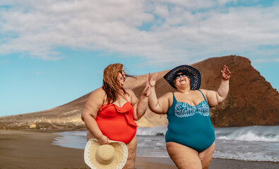 Happy plus size women having fun walking on the beach during summer vacations - Overweight people...