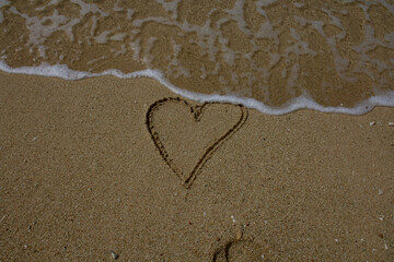 Heart on the beach. The sea wave washes away the heart drawn on the sand.