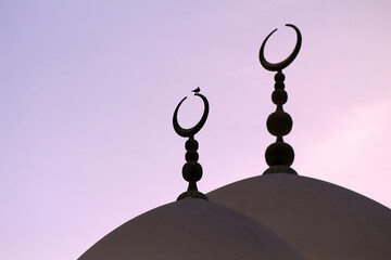 The dome of a mosque showing the crescent moon silhouetted at sunset.