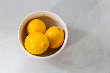 Selective focus flat lay side lit view of three fresh lemons in white lightly speckled bowl on ceramic background