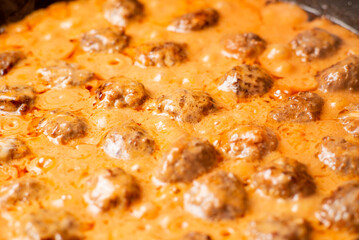 Cooking homemade meatballs in a frying pan in a sauce of tomatoes and sour cream. Close-up macro. Food background.