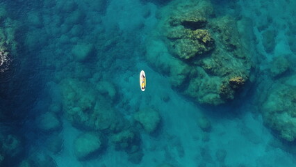 Fototapeta na wymiar A man lies on a Supboard in the Mediterranean sea with stones at the bottom of the sea from a drone