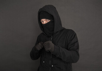 Unrecognizable man in the black hoody with hood wearing balaclava mask holding his fists near chest