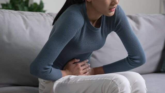 Young Asian woman having a stomach ache. Menstrual period cramp, abdominal pain, food poisoning. Health care and medical concept.