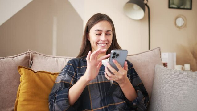 Close up overjoyed happy woman looking at phone screen, celebrating success, showing yes gesture, sitting at home. Young female excited by good news in email or message, job promotion, money refund.