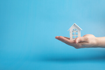 Fototapeta na wymiar hand holding a house, real estate services, construction and repair, blue background, copy space