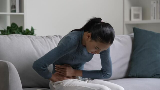 Young Asian woman having a stomach ache. Menstrual period cramp, abdominal pain, food poisoning. Health care and medical concept.