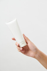 흰색 튜브 형태의 화장품 목각 모형을 들고 있는 20대 여성의 손