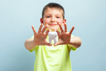 Child shows big white toy tooth on a blue background. Caring for teeth