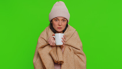 Sick woman wear hat wrapped in plaid shivering from cold, drinking hot tea in unheated apartment...