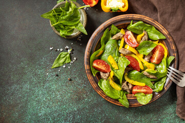 Warm salad from the baby spinach, chicken liver, tomatoes and peppers with spices and balsamic on stone background. View from above. Copy space.