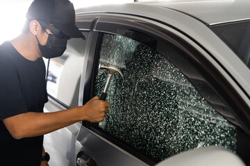 Thief with mask breaking car window with hammer on day time. Car thief, car theft concept.