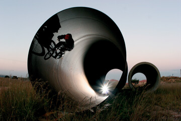 A BMX rider silhouetted as he rides inside a huge metal pipe.