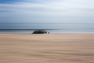 Fototapeta na wymiar Hard rock. An isolated rock on a beach with a path blur abstract edit.