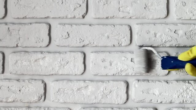 Painting the wall with a brush. Repair with your own hands at home. Texture of decorative gypsum brick for the planning a loft interior. Construction work. Builder's hand with paint brush