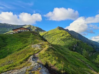 Majestic summer alpine resort with hut on the green fields and green mountains in background, panorama of European Alps "Hohe Tauern" 