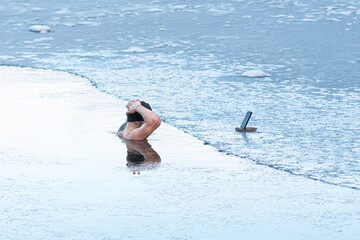 Boy or man with warm hat and a smartphone on the ice bathing in the cold water of a lake. Wim Hof...