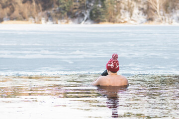 Fototapeta na wymiar Man or boy with a warm hat and gloves ice bathing in the cold water of a lake. Wim Hof Method, cold therapy, breathing techniques, yoga and meditation