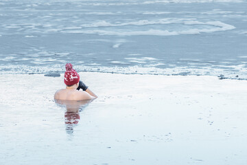 Man or boy with a warm hat and gloves ice bathing in the cold water of a lake. Wim Hof Method, cold therapy, breathing techniques, yoga and meditation