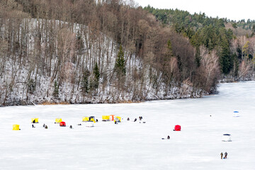 Fishermen fishing on a frozen lake in winter with fishing pole or rod, ice auger, various equipment...