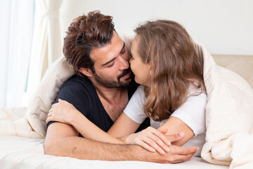 Young couple in a relationship kissing and cuddling. Happy couple hug and kiss on the bed near the window in the morning. Sensual young couple kissing on bed at home.