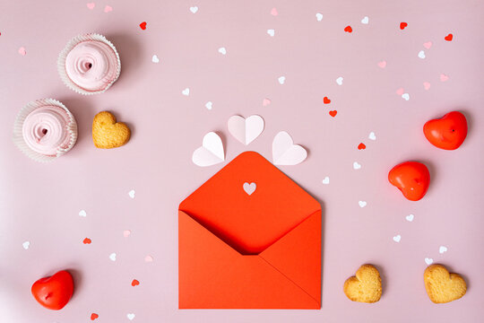 an open empty red envelope with a heart lies in the center on a pink background, heart-shaped cookies, white paper valentines, confetti, red candles, pink marshmallows lie nearby - Powered by Adobe