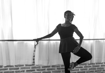 A Black American female dancer, holding a ballet position on the barre at a dance studio in Bali, Indonesia
