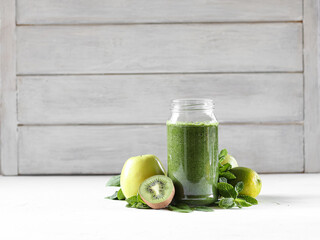Green smoothie with spinach, banana, kiwi, mint and apple, poured into a glass jar. Near fruit and greens.
