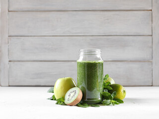 Green smoothie with spinach, banana, kiwi, apple and mint in a glass jar on the wooden background. 
