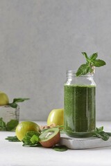 Green smoothie with spinach, banana, kiwi, apple and mint in a glass jar decorated with mint. Delicious and healthy breakfast.

