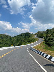 Small road surrounded by green forest and blue sky, perfect for outdoor and travel projects. Scenic summer landscape, ideal as background. Tranquil nature image transports audience to peaceful place.