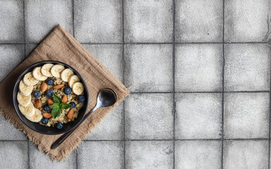 Oatmeal with banana, blue and nuts lies in a black plate, which stands on a beige napkin, next to it lies a spoon. Healthy breakfast.

