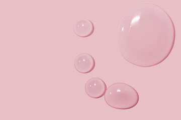 large drops of cosmetic serum, liquid, water, gel on a pink background