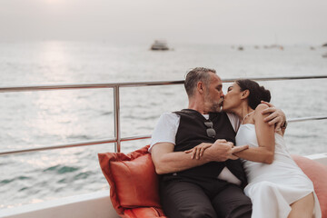 Romantic couple love kissing on yacht. Happy man and woman sitting on side of boat and hugging in...